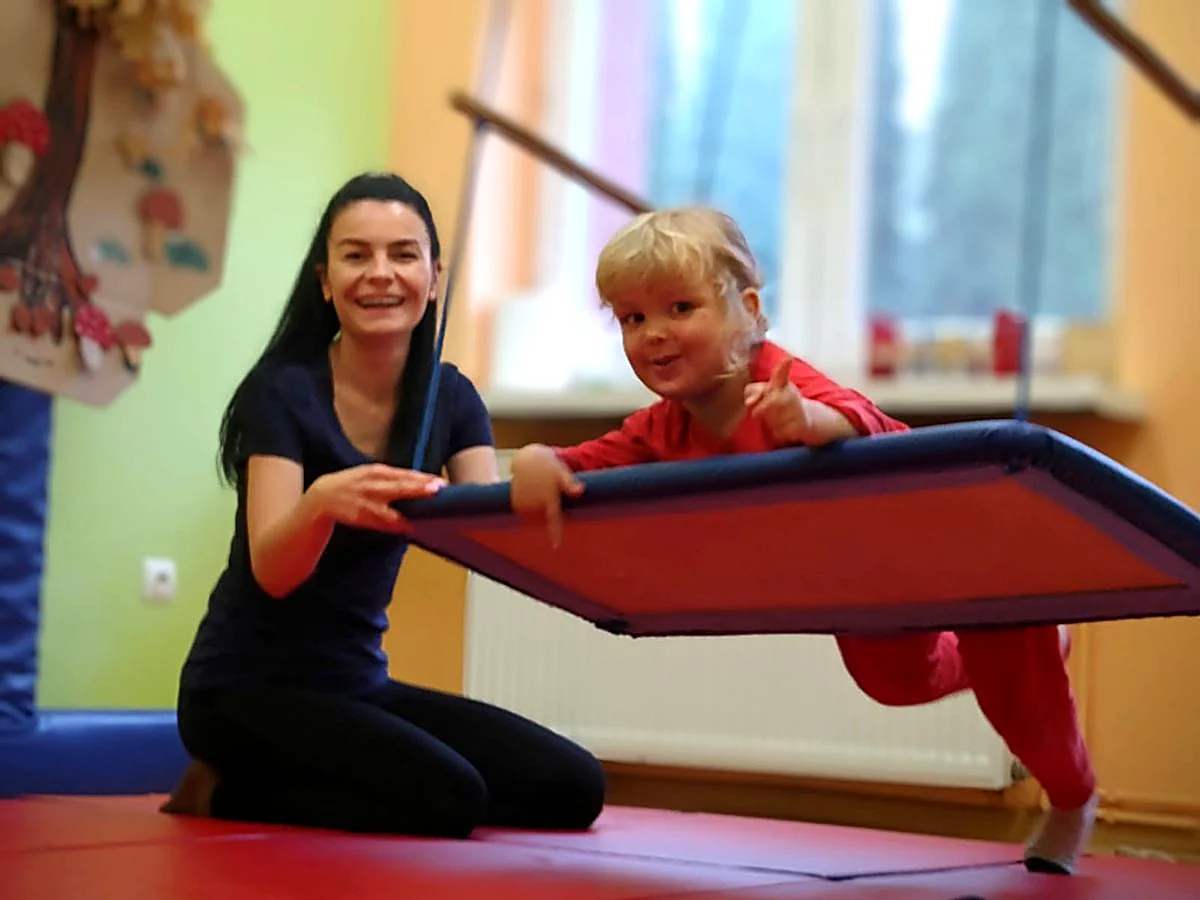 Roześmiane dziecko na huśtawce terapeutycznej z uśmiechniętą terapeutką